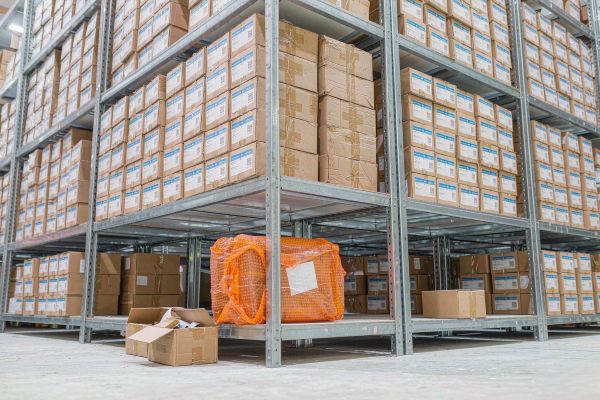 Stacked cartons of bulk challenge coin orders on shelves contrasted with one small parcel