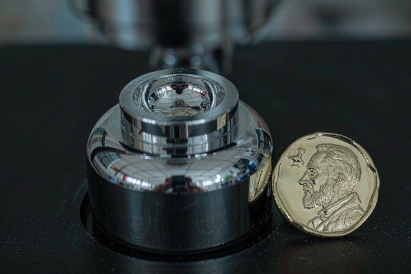 A polished steel challenge coin die beside a freshly struck custom coin on a dark workbench